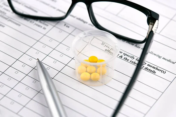 Brille, gelbe Pillen im Glas und Stift auf medizinischen Geräten — Stockfoto