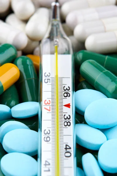 Thermometer on blue pills and colorful capsules. Medicine Stock Picture