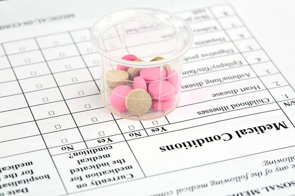 Розовые и коричневые таблетки в оконченном стекле на медицинской анкете — стоковое фото