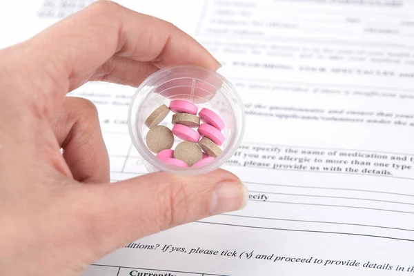 Colorful pills in hand and medical questionnaire form on background