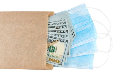 Mavi tıbbi yüz maskeleri ve beyaz arka planda izole edilmiş kahverengi kağıt pakette 100 dolarlık banknotlar.