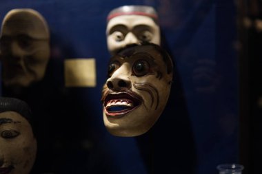 Traditional Indonesian mask with a man's face and visible teeth displayed on a display shelf for educational purposes.