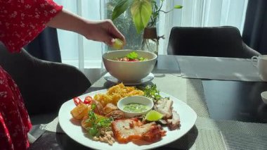 Bir el, Bangkok 'taki bir lokanta masasında bir kase Kuzey Tayland usulü körili eriştenin üzerine taze limon sıkıyor. Hem de gün ışığında. Yüksek kalite 4k görüntü