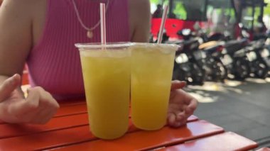 Baston şeker kamışı ya da şeker kamışı suyu satıcısı. Elinde iki bardak baston suyu tutan bir kız masada motosikletlerin arka planında oturuyor. Yüksek kalite 4k görüntü