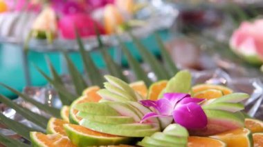 Yakından çekilen bir el, olgun yaban mersinleriyle dolu, dağınık kayısılar ve beyaz ahşap bir masada çiçek düzeniyle çevrili kırsal ahşap bir tabağı almak için uzanan bir el yakalıyor. .