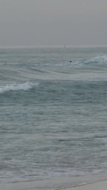 Köpüklü deniz dalgaları kumsala geliyor güneşli yaz güneşinde güzel turistleri silip süpürüyor. Yüksek kalite 4k görüntü