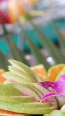 Yakından çekilen bir el, olgun yaban mersinleriyle dolu, dağınık kayısılar ve beyaz ahşap bir masada çiçek düzeniyle çevrili kırsal ahşap bir tabağı almak için uzanan bir el yakalıyor. .