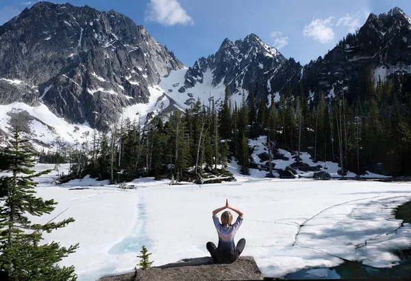 Inner peace and mindfulness. Woman meditating on scenic lake shore with beautiful view of snow covered mountains. Colchuck Lake. The Enchantments. Leavenworth. Washington State. United States of America.
