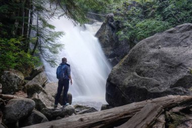 Kadın yakınındaki kayaların üzerinde duran şelaleler. Whistler bahar tatil. Gökkuşağı Falls gökkuşağı Nehri üzerinde. Garibaldi Provincial Park. Whistler. British Columbia. Kanada.