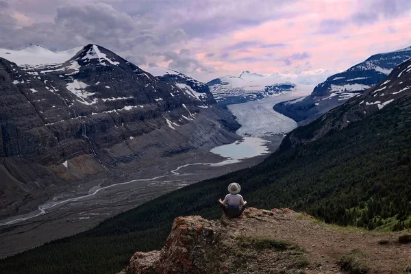 Woman meditating on steep cliff over Columbia Icefield glacier and a moraine lake.  Outdoor yoga in  Banff / Jasper National Park. Canadian Rocky Mountains.  Patterson Ridge trail. Alberta. Canada.