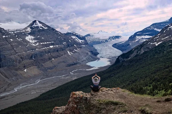 Woman meditating on steep cliff over Columbia Icefield glacier and a moraine lake.  Outdoor yoga in  Banff / Jasper National Park. Canadian Rocky Mountains.  Patterson Ridge trail. Alberta. Canada.