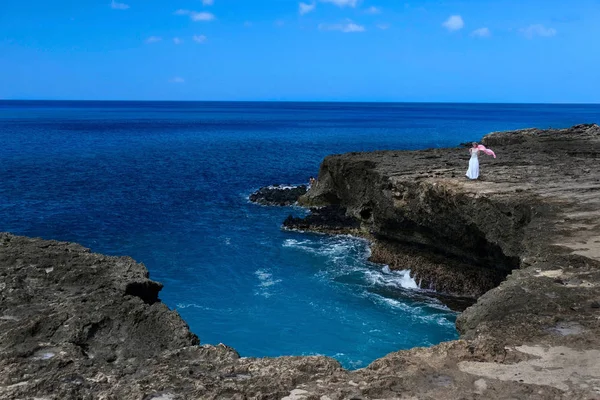 Vacation on Hawaii. Middle age woman standing on a volcanic rock cliff above the ocean with her scarf flying in the wind. Kaena Point Park. Honolulu. Hawaii. USA