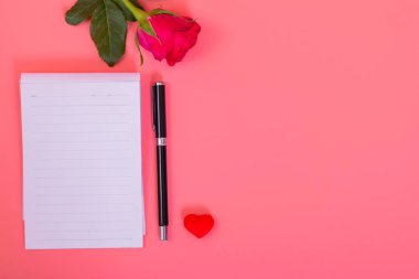 Pembe güllerle dolu kalp kutusunda bir sürü küçük kalp, pembe arka planda bir kalem.