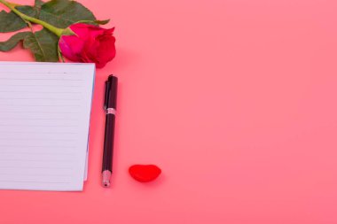 Pembe güllerle dolu kalp kutusunda bir sürü küçük kalp, pembe arka planda bir kalem.