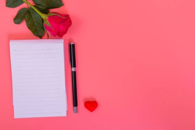 Pembe güllerle dolu kalp kutusunda bir sürü küçük kalp, pembe arka planda bir kalem.