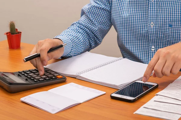 Hesap makinesi kullanan ve faturaları akıllı telefon kullanarak ödeyen bir adam. Ödeme kredi kartı.