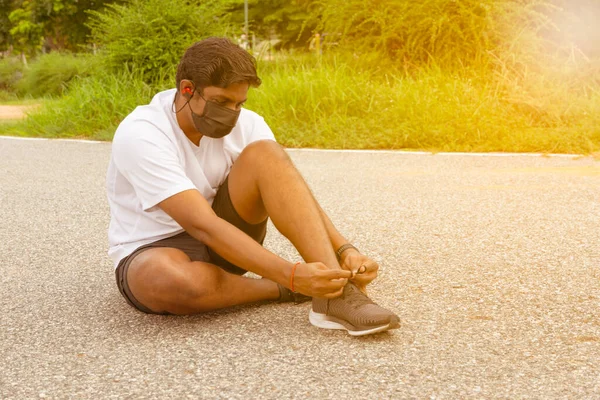 Young attractive man model in white shirt tying laces on his running shoes with copy space
