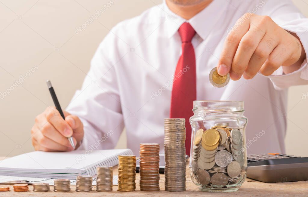 Hand of male putting coins in jar with money stack step growing growth saving money with gray background