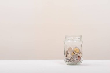 Kavanozda bozuk para ya da yumuşak beyaz arka planlı cam şişe. Para biriktirme, tasarruf kavramı