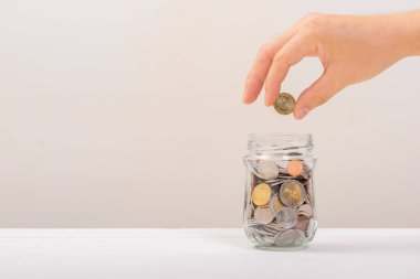 Beyaz adam, altın sikkeyi kavanozun içine koymak için tutuyordu ya da beyaz arka planda biriktirmek için cam şişeyi. Para biriktirme, tasarruf kavramı