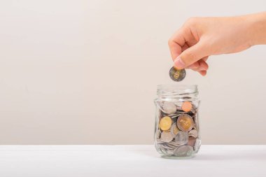 Beyaz adam, altın sikkeyi kavanozun içine koymak için tutuyordu ya da beyaz arka planda biriktirmek için cam şişeyi. Para biriktirme, tasarruf kavramı
