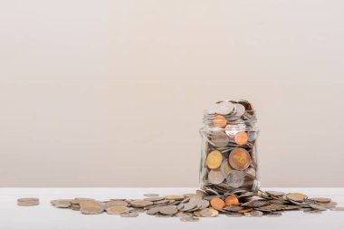 Kavanozda bozuk para ya da yumuşak beyaz arka planlı cam şişe. Para biriktirme, tasarruf kavramı