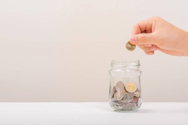 Beyaz adam, altın sikkeyi kavanozun içine koymak için tutuyordu ya da beyaz arka planda biriktirmek için cam şişeyi. Para biriktirme, tasarruf kavramı