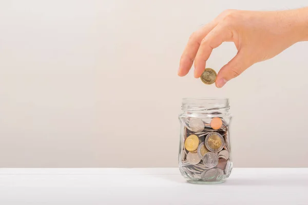 Beyaz adam, altın sikkeyi kavanozun içine koymak için tutuyordu ya da beyaz arka planda biriktirmek için cam şişeyi. Para biriktirme, tasarruf kavramı