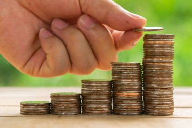 Beyaz adam masasına para koymak için bozuk para tutuyor ve fındık yeşili bokeh arkaplan kullanıyor. Para tasarrufu kavramı veya İş Büyümesi kavramı.