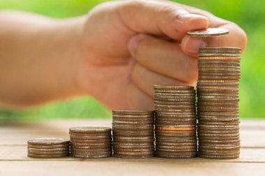 Beyaz adam masasına para koymak için bozuk para tutuyor ve fındık yeşili bokeh arkaplan kullanıyor. Para tasarrufu kavramı veya İş Büyümesi kavramı.