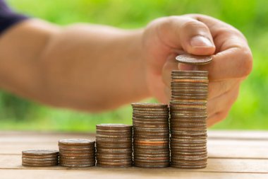 Beyaz adam masasına para koymak için bozuk para tutuyor ve fındık yeşili bokeh arkaplan kullanıyor. Para tasarrufu kavramı veya İş Büyümesi kavramı.