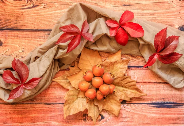 A pile of ripe medlar on a golden leaves and red leaves around them on wooden background, top view