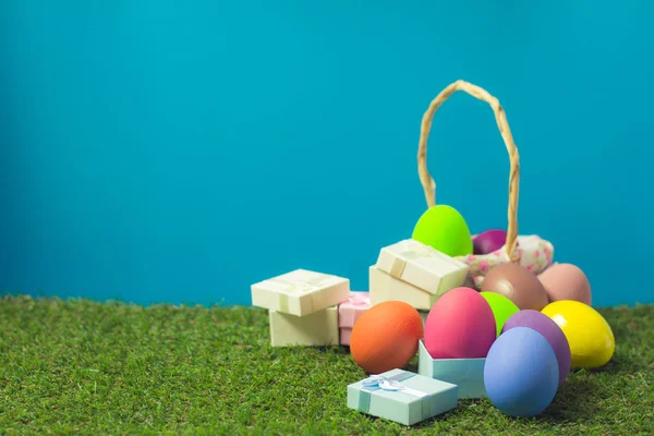Huevos de Pascua en una cesta tejen madera y caja de regalo en el gra verde — Foto de Stock