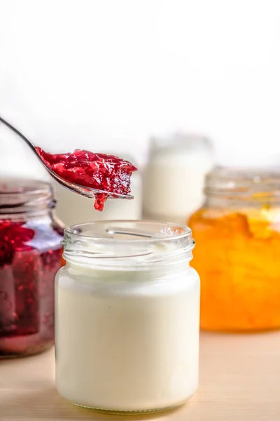 Homemade yogurt with orange jam spoon eating from a glass jar. Healthy dairy probiotic breakfast.