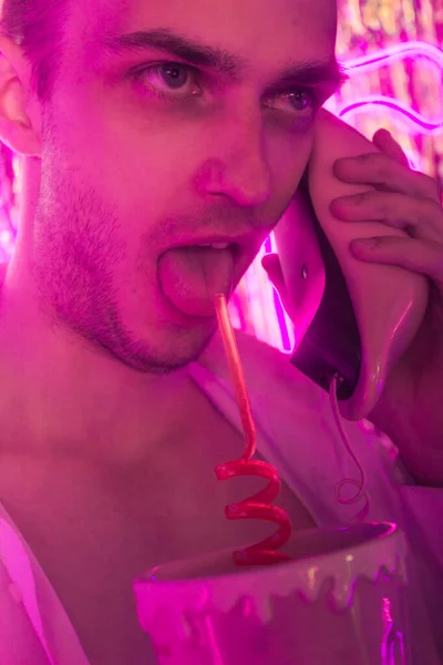 Genç Yakışıklı 'nın portresi ve yeni bir telefon. Neon renkli oda. Eski 90 'lar eski moda. Erkeğe yakın neon kelimelerin yansıması.