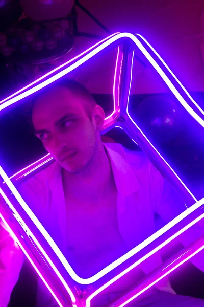 Düğmeleri iliklenmemiş beyaz gömlekli yakışıklı adamın portresi. Neon renkli oda. Eski 90 'lar eski moda. Erkeğe yakın neon kelimelerin yansıması.