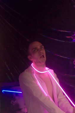 Düğmeleri iliklenmemiş beyaz gömlekli yakışıklı adamın portresi. Neon renkli oda. Eski 90 'lar eski moda. Erkeğe yakın neon kelimelerin yansıması.