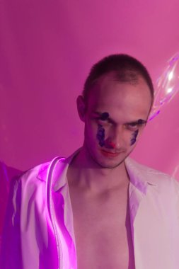 Düğmeleri iliklenmemiş beyaz gömlekli yakışıklı adamın portresi. Neon renkli oda. Eski 90 'lar eski moda. Erkeğe yakın neon kelimelerin yansıması.