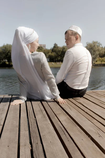 Couple young muslim man and woman sittin on wooden stairs near the lake. Muslim tatar wedding.