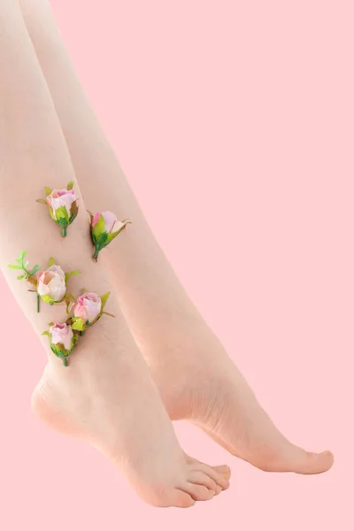 Γυναίκες λεπτό αξύριστο πόδι με ροζ λουλούδια σε ροζ φόντο. Φεμινισμός — Φωτογραφία Αρχείου