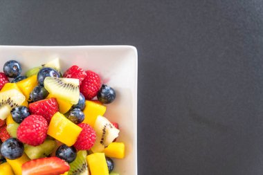 Beyaz tabakta karışık taze meyve (çilek, ahududu, yaban mersini, kivi, mango)