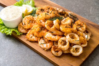 Tahta üzerinde sos olan kızarmış deniz ürünleri (mürekkep balıkları, karidesler, midyeler)