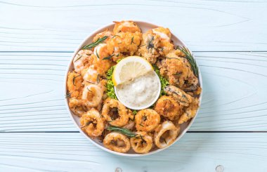 Tahta üzerinde sos olan kızarmış deniz ürünleri (mürekkep balıkları, karidesler, midyeler)