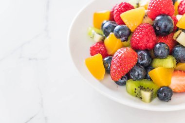 Beyaz tabakta karışık taze meyve (çilek, ahududu, yaban mersini, kivi, mango)