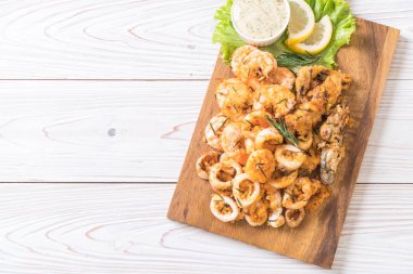 Tahta üzerinde sos olan kızarmış deniz ürünleri (mürekkep balıkları, karidesler, midyeler)