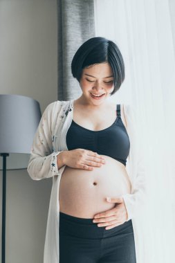 Genç güzel Asyalı hamile kadın ona dokunan karın evde - vintage filtre stili ile seçici odak noktası