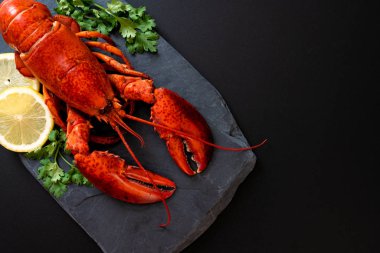 Sebzeli kırmızı ıstakoz ve siyah tabakta limon.