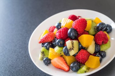 Beyaz tabakta karışık taze meyve (çilek, ahududu, yaban mersini, kivi, mango)