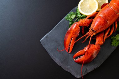 Sebzeli kırmızı ıstakoz ve siyah tabakta limon.