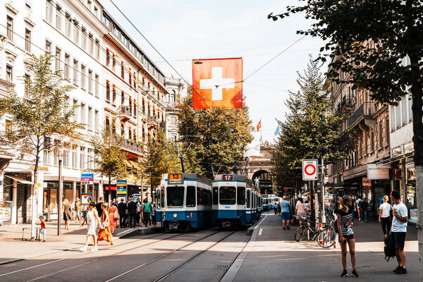 ZURICH, SWITZERLAND - AUG 23, 2018: A tram drives down the center of Bahnhofstrasse while people walk on the sidewalks in Zurich City, Switzerland.